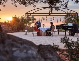 Romance fills the air as lanterns hang from a gazebo while a waiter pours wine for a couple serenaded by a grand piano