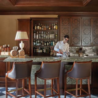 Barman mixing a cocktail at a green marble counter fronted by leather barstools