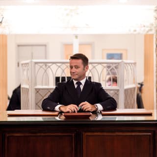Concierge at a polished wooden hotel reception desk looking towards the camera