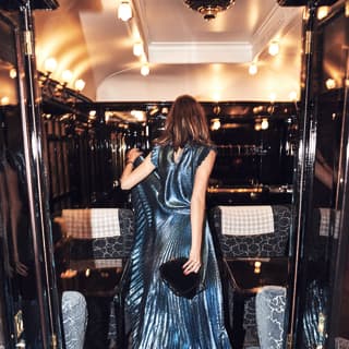 Lady in a metalic blue crépe dress walking along a vintage train carriage