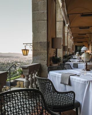 As evening sets in, table lights along the interior wall of the loggia come on, illuminating an elegant restaurant ready for guests